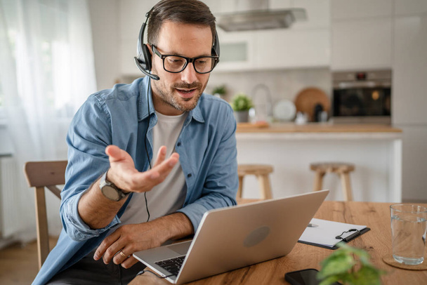 Um homem caucasiano masculino freelancer trabalho de casa com fones de ouvido na cabeça no computador portátil suporte ao cliente despachante - Foto, Imagem