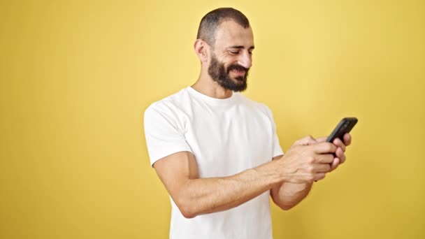 Jonge Spaanse man met behulp van smartphone glimlachen over geïsoleerde gele achtergrond - Video