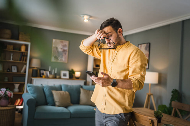 Um homem adulto caucasiano macho com barba e óculos ficar em casa sorriso feliz usar smartphone telefone móvel para enviar mensagens de texto SMS ou navegar no espaço de cópia on-line internet - Foto, Imagem