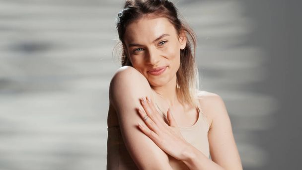 Caucasian lady promoting body cream in studio, filming beauty ad campaign and applying moisturizer and neck and shoulders. Beautiful model using glowing serum and advertising product. - Photo, image