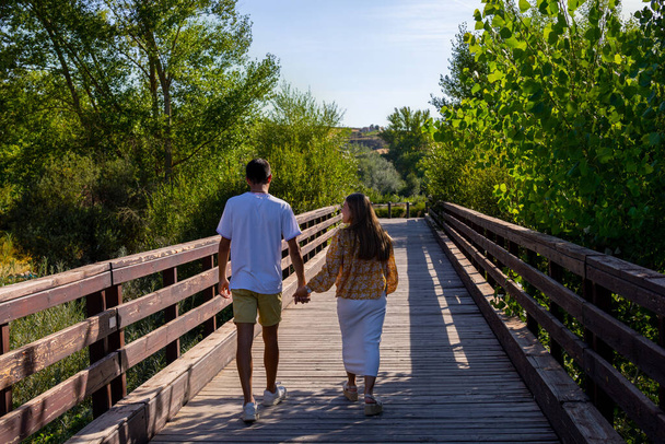 chłopiec i dziewczyna w miłości spacery wzdłuż drewnianego mostu trzymając się za ręce w słoneczny dzień z ostrością selektywne - Zdjęcie, obraz