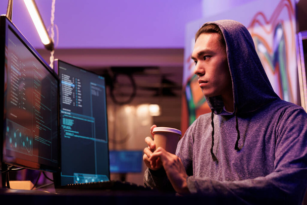 Ázsiai hacker kávézik és dos támadást csinál a honlapon. Bűnöző betört a hálózati rendszerbe a számítógép képernyőjén, miközben italokat tartott, hogy bemenjen egy elhagyatott raktárba. - Fotó, kép