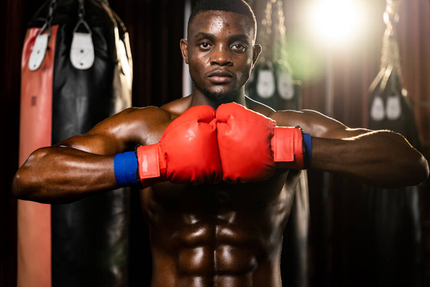 Combattant de boxe posant, le boxeur noir afro-américain a mis sa main ou son poing en portant un gant devant lui dans une position agressive et prêt à se battre au gymnase avec un sac à pied et un équipement de boxe. Impulsion - Photo, image