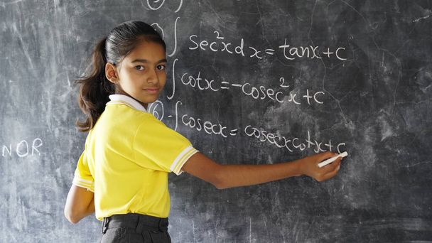 Glückliches indisches Schulmädchen, das vor schwarzem Tafelhintergrund steht. Bildungskonzept oder Zurück in die Schule - Foto, Bild