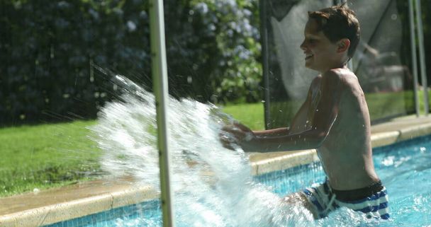 Хлопчик у басейні розбризкує воду за межами басейну. Дитина бризкає воду рукою
 - Фото, зображення