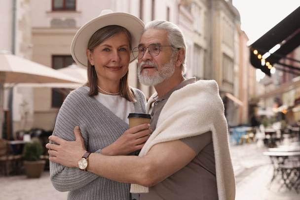 Affectionate senior couple with coffee walking outdoors - Foto, afbeelding