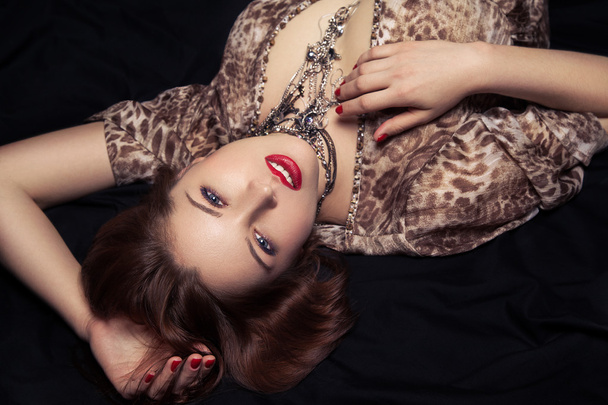 High fashion blik. Glamour close-up portret van mooie sexy stijlvolle vrouw model liggend op zwarte bed met lichte make-up, met rode lippen, met perfect schoon op bed - Foto, afbeelding