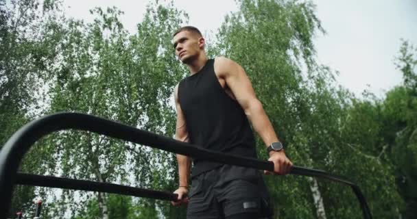 Athletic man has workout, hanging and pull up on parallel bars outdoors. Young sporty male with muscular body exercising on sport ground at park. - Footage, Video