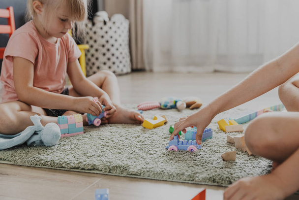 Dzieci bawiące się kolorowym plastikowym zabawką kolorowy pociąg. Dzieci siedzące na dywanie w pomieszczeniach w słonecznej białej sypialni lub przedszkolu, pokoju dziecinnym. Zabawna edukacja ekologiczna gra dla dzieci - Zdjęcie, obraz