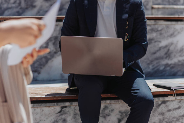 Photo recadrée d'un homme d'affaires assis dans un escalier à l'extérieur et travaillant sur un ordinateur portable - Photo, image
