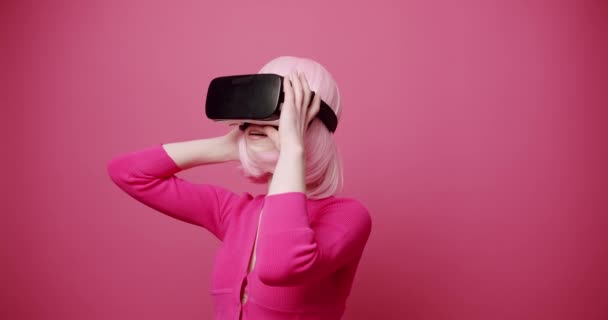 Nainen käyttää virtuaalitodellisuus lasit, etsiä ja koskettaa virtuaalista elämää eristetty vaaleanpunainen tausta. Tulevaisuuden käsite, innovaatio, teknologia, pelaaminen, elämäntapa, viihde. Vaaleanpunaiset värit. Moderni nainen - Materiaali, video