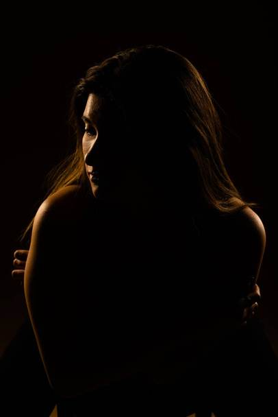 Een silhouet foto van een prachtig meisje poserend in de studio terwijl zittend op een stoel - Foto, afbeelding
