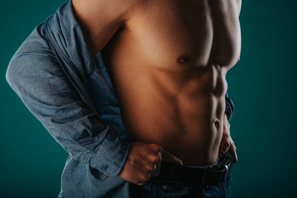 Jovem homem musculoso com uma parte superior do corpo meia nua posando no estúdio com os braços na cintura - Foto, Imagem