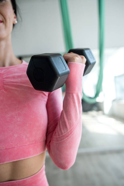 Slanke vrouwelijke atleet doet oefeningen met halters in de fitnessruimte. Sportconcept - Foto, afbeelding