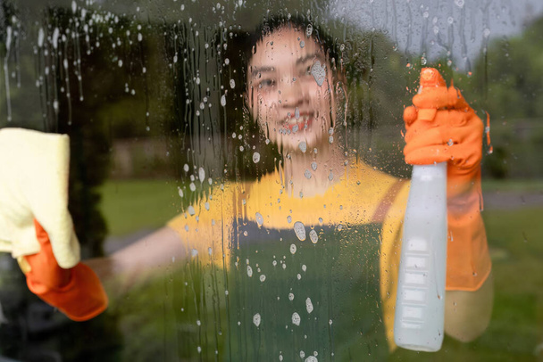 Nettoyage de la maison d'une femme au foyer qui essuie le verre à l'aide d'un spray nettoyant et d'un chiffon. - Photo, image