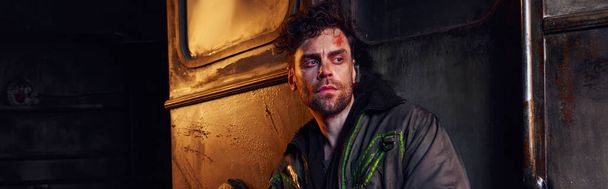 отчаявшийся мужчина в изношенной куртке смотрит в темноте постапокалиптического опустошенного метро, знамя - Фото, изображение