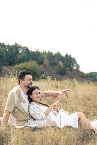 Счастливые женатые мужчина и женщина на свидании расслабляясь в поле летом, качественное время вместе, близкие отношения, романтика в браке. - Фото, изображение