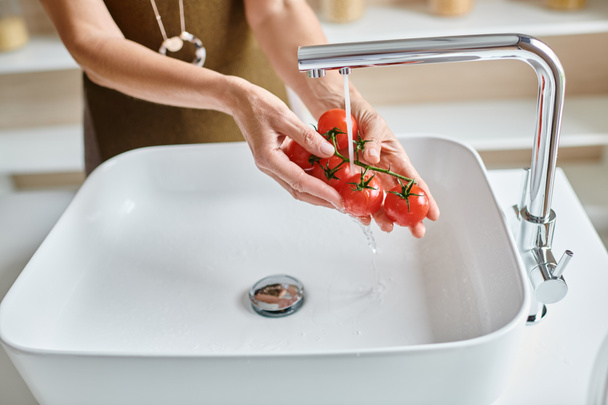 обрізаний знімок жінки, що миє свіжі та стиглі вишневі помідори вдома, жіночі руки тримають овочі - Фото, зображення