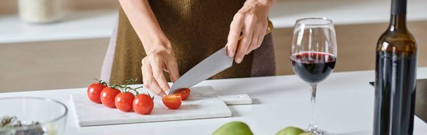 donna ritagliata che taglia pomodorini freschi vicino al bicchiere di vino rosso, avocado e mele verdi, striscione - Foto, immagini