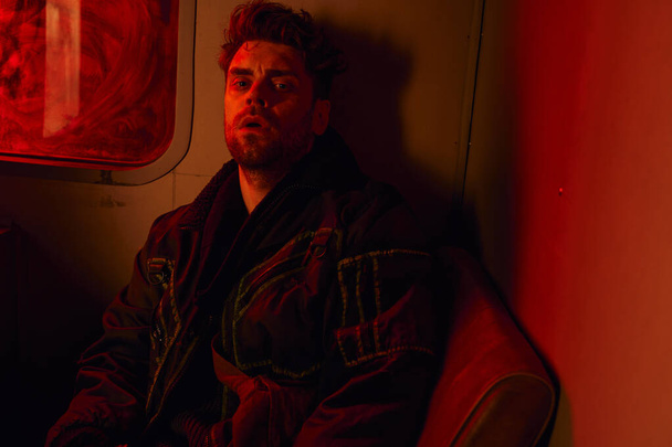 измученный человек, сидящий в красном свете грязной кареты постапокалиптического метро, игровой персонаж - Фото, изображение