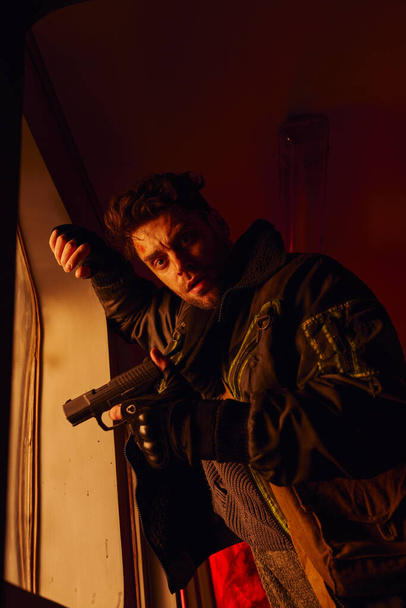 fronsen ongeschoren man met pistool kijken naar camera in metro rijtuig in post-apocalyptische metro - Foto, afbeelding