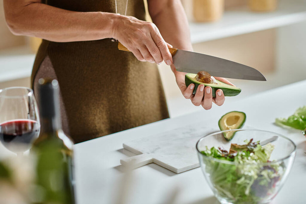 Teilweise Schuss, Frau schneidet frische Avocado in der Nähe von Kirschtomaten und Salat in Schüssel, Hausmannskost - Foto, Bild