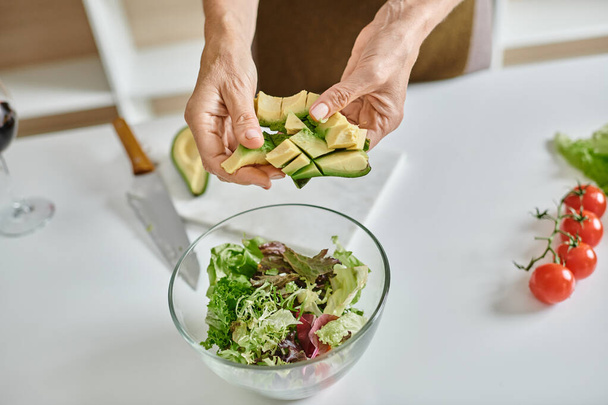 zugeschnittene Frau mit in Scheiben geschnittener reifer Avocado in der Nähe von Salat in Schüssel und Glas Rotwein, Nahaufnahme - Foto, Bild