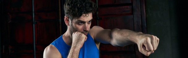confident unshaven man in blue tank top training and boxing on city street at night - Photo, Image