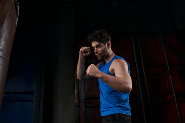 confident unshaven man in sportswear working out with punching bag on street at night - Foto, Imagem