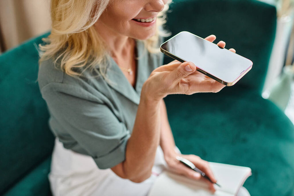 обрезанная счастливая женщина средних лет записывает голосовой массаж и держит ручку рядом с ноутбуком - Фото, изображение