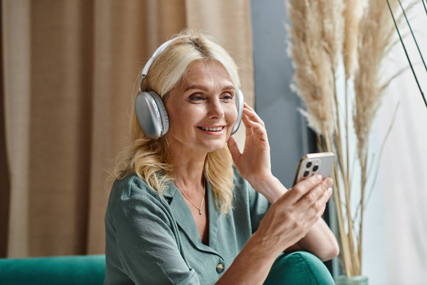 radosna kobieta w średnim wieku w słuchawkach bezprzewodowych słuchanie muzyki i korzystanie ze smartfona w domu - Zdjęcie, obraz