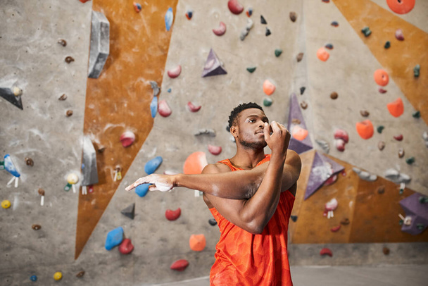 atletyczny Amerykanin w pomarańczowej koszuli rozgrzewa się przed wspinaczką na ścianę, wspinaczka skalna - Zdjęcie, obraz