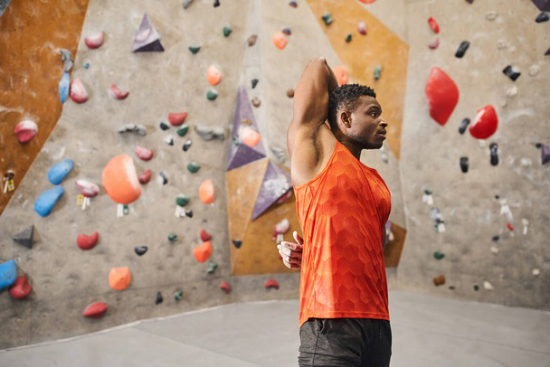 Turuncu tişörtlü Afro-Amerikan atletizm adamı elleri arkada ısınıyor, tırmanma konsepti - Fotoğraf, Görsel