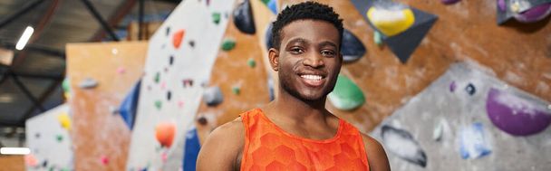 joyful african american man smiling cheerfully at camera with rock climbing wall backdrop, banner - Photo, Image