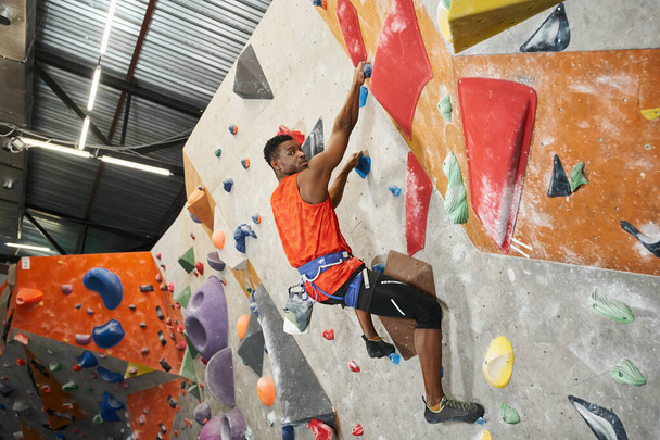 atlétikai afro-amerikai férfi pózol profil alpesi hámot mászás és nézi a kamera - Fotó, kép