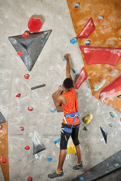 plan vertical de sportif afro-américain accroché au bout des doigts sur un mur de roche, vue de dos - Photo, image
