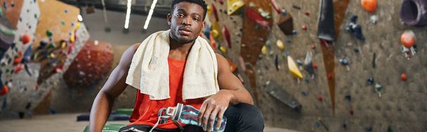 спортивний афроамериканський чоловік в аварійному килимку з рушником на плечах дивиться на камеру, банер - Фото, зображення