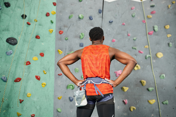 visszapillantás sportos afro-amerikai férfi kész felmászni sziklafal kezével csípő - Fotó, kép