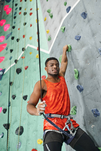 handsome african american man posing while ascending up bouldering wall using safety rope, sport - Photo, Image