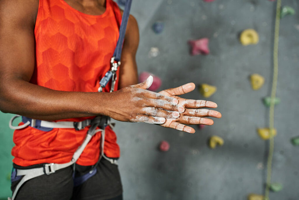 vista recortada de las manos en talco en polvo del joven afroamericano en camisa naranja con cuerda de seguridad - Foto, Imagen