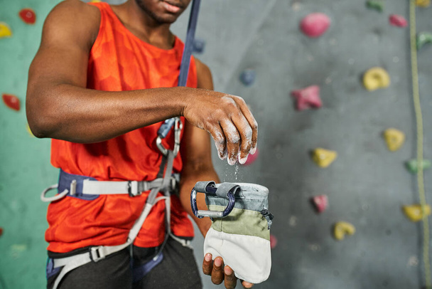 przycięty widok afrykańskiego Amerykanina za pomocą kredy siłowni na jego sprzęt wspinaczkowy, bouldering - Zdjęcie, obraz