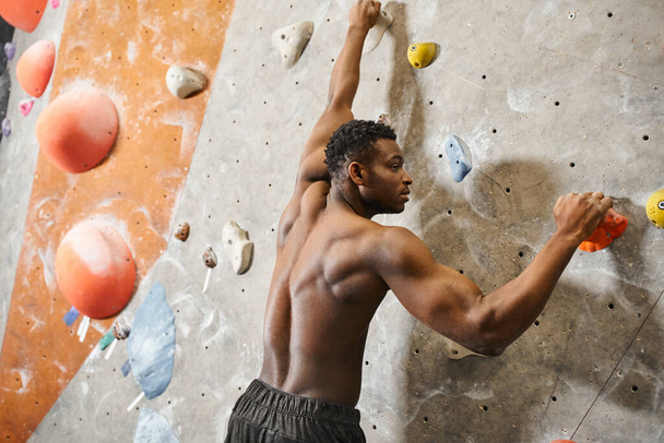 back view of athletic young african american man with his shirt off climbing up bouldering wall - Photo, Image