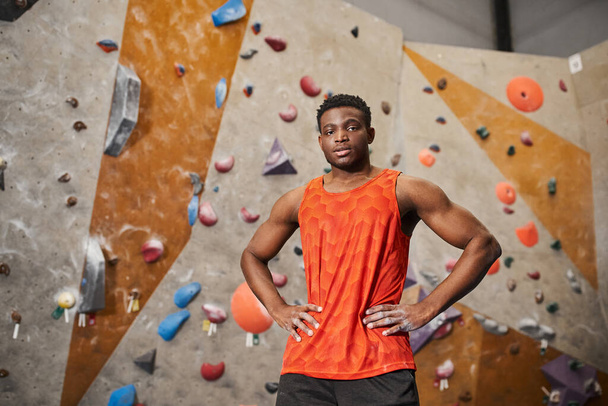 gut aussehender junger afrikanisch-amerikanischer Mann in orangefarbenem Hemd posiert mit den Händen auf den Hüften und blickt in die Kamera - Foto, Bild