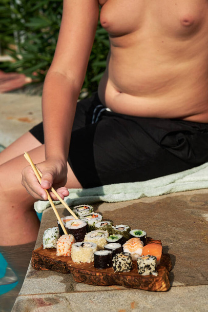 Niño en traje de baño con un plato de sushi junto a la piscina - Foto, Imagen