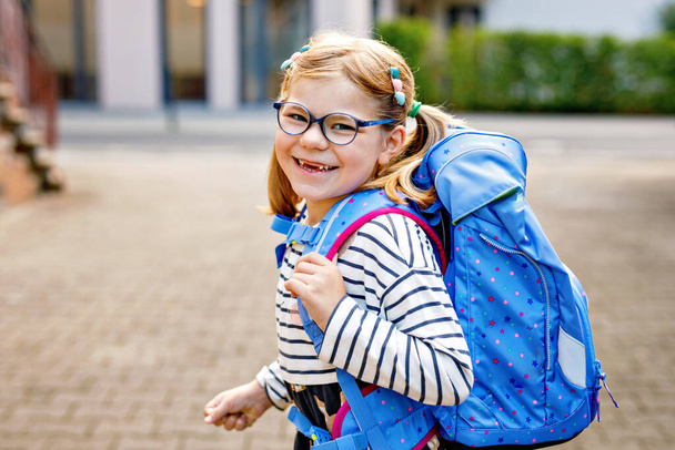 Söpö tyttö ensimmäisenä koulupäivänään. Terveellinen kaunis lapsi kävelee esikouluun ja päiväkodille. Onnellinen lapsi silmälasien kanssa reppu kaupungin kadulla, ulkona - Valokuva, kuva