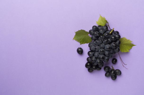 Bunch of ripe dark blue grapes with leaves on color background, top view. - Photo, Image