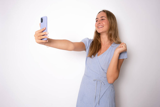 Retrato de una mujer casual sonriente sosteniendo el teléfono inteligente sobre fondo blanco - Foto, imagen
