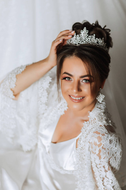 Gorgeous bride portrait in her robe wearing tiara. Beautiful bridal makeup and hairstyle and hair accessories. Bride to be smiling portrait - Foto, afbeelding