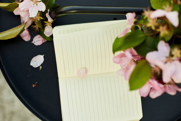 Open notebook en bloemen en op de kleine zwarte tafel op het terras thuis in een zonnige dag, buiten werkruimte, zomer ontspanning, notities, ideeën, plannin - Foto, afbeelding