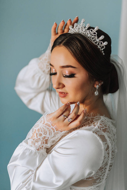 A wonderful portrait of a bride in a robe with a tiara on her head. Beautiful wedding makeup, hairstyle and hair accessories. Bride smiling, portrait - 写真・画像